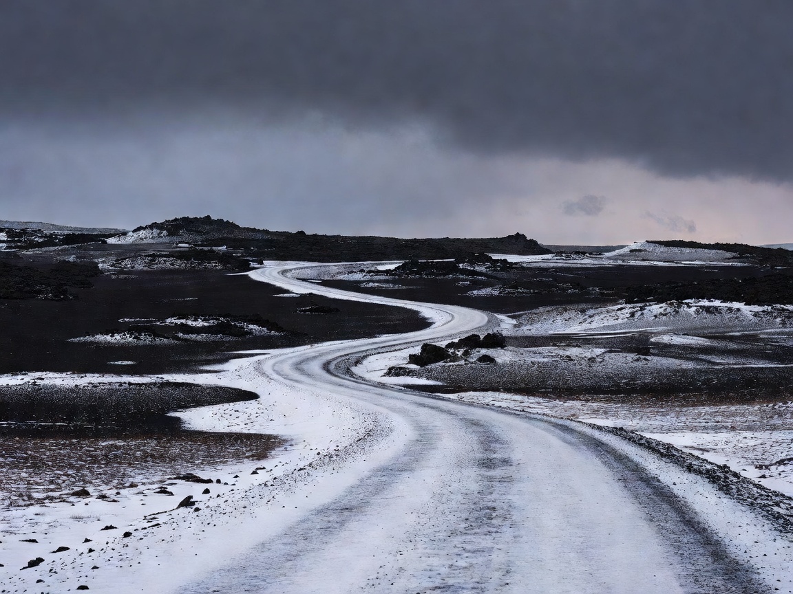 Snow-dusted Icelandic road crossing a dark volcanic landscape beneath winter clouds